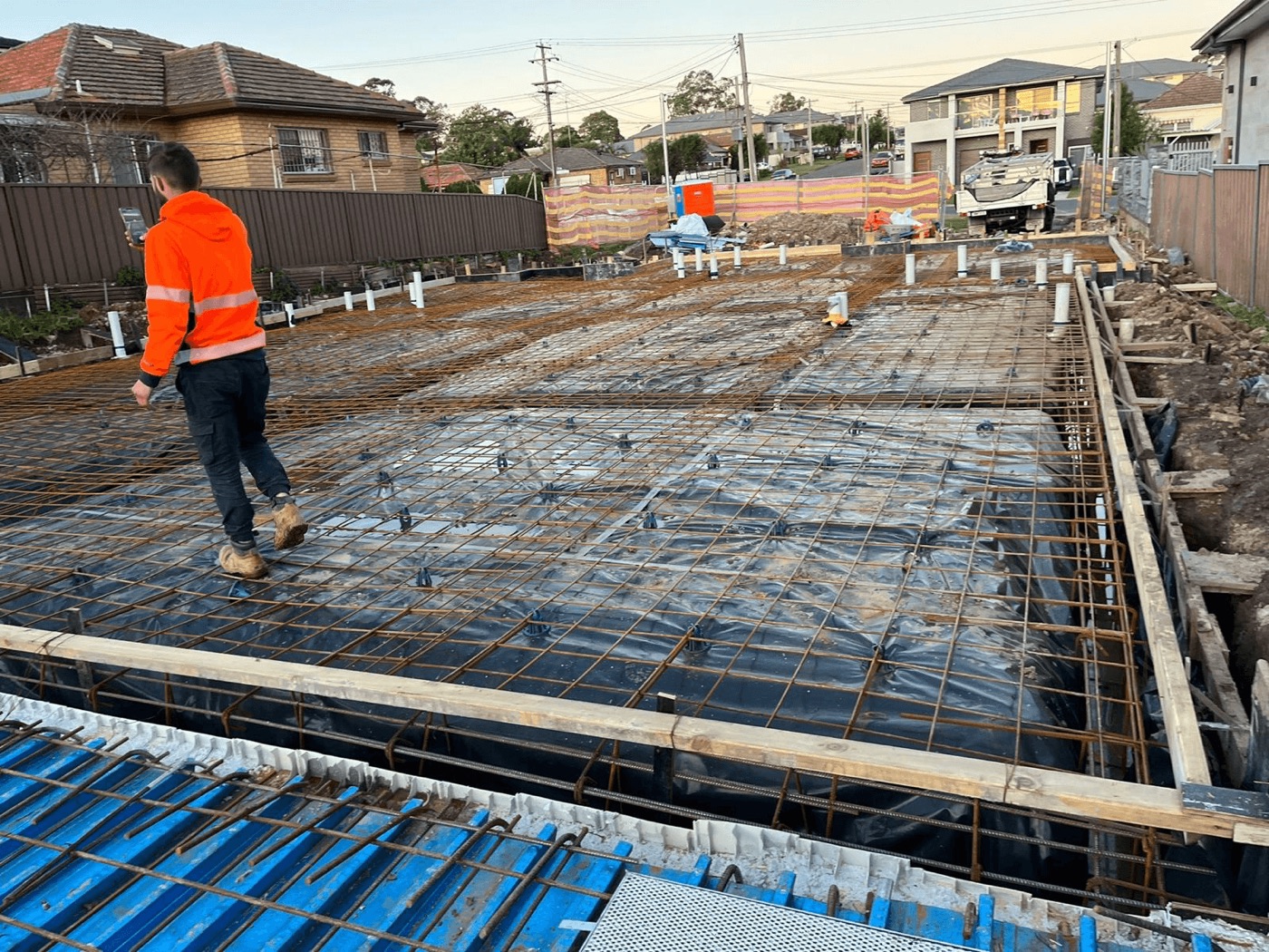 Raft slab with dense steel reinforcement mesh over black membrane — worker inspecting on a Sydney building site